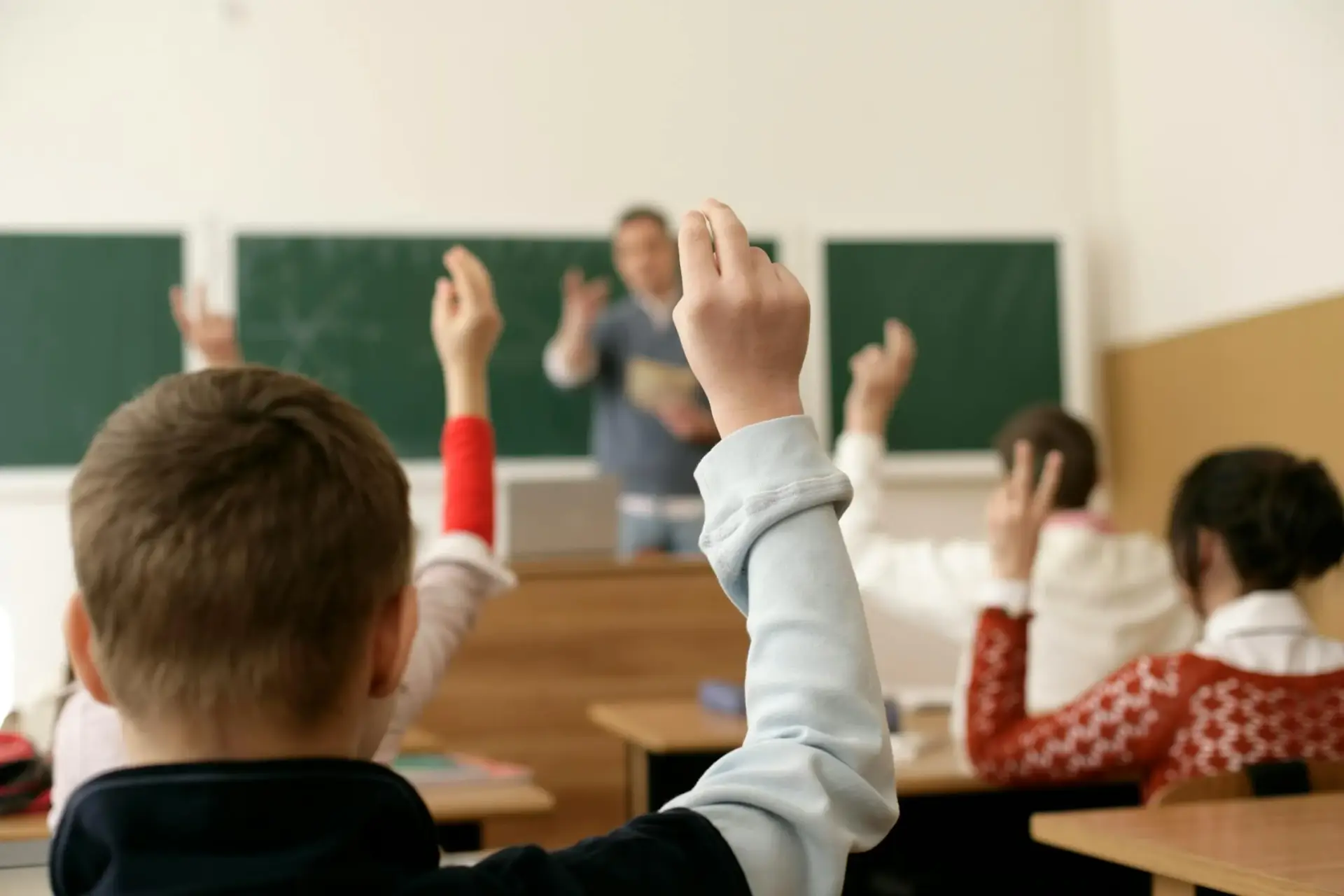 Volunteer teaching a classroom of students with their hands raised, engaging in an interactive learning session.