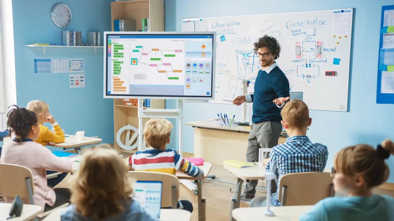 Teacher using a smart board to conduct an interactive lesson in a modern classroom, with students engaged through digital devices.